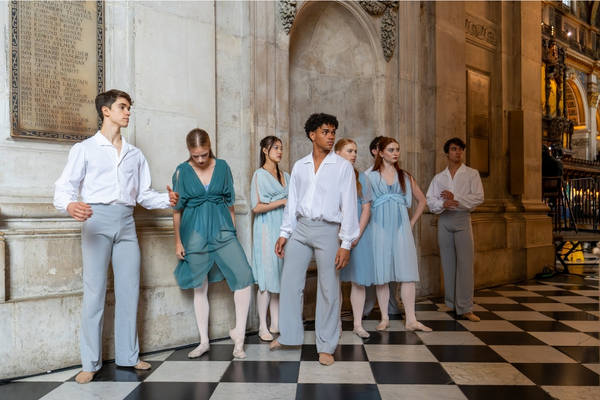 Student choreography shines at benefact group’s service of celebration at st paul's cathedral The eight dancers stand on the sidelines of the cathedral in flowy fabrics. The ladies wear teal and light blue sheer mesh tunics over matching colour leotards, pink tights and flat ballet shoes. The men wear white flowy button down shirts with long-sleeves, light grey trousers and skin-tone ballet shoes.