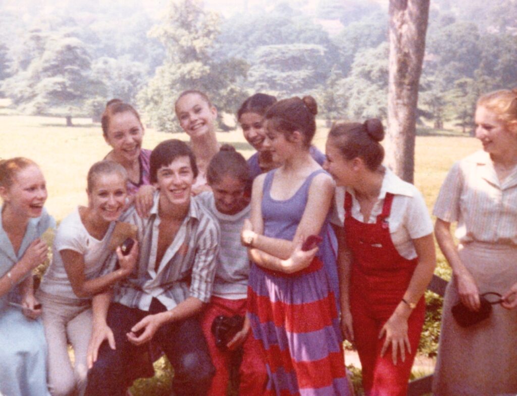 100 stories: christopher saunders A group of students in regular clothes sit for a group photo outside in richmond park. The girls' hair are still in buns. Some smile at christopher while christopher and a few others smile at the camera