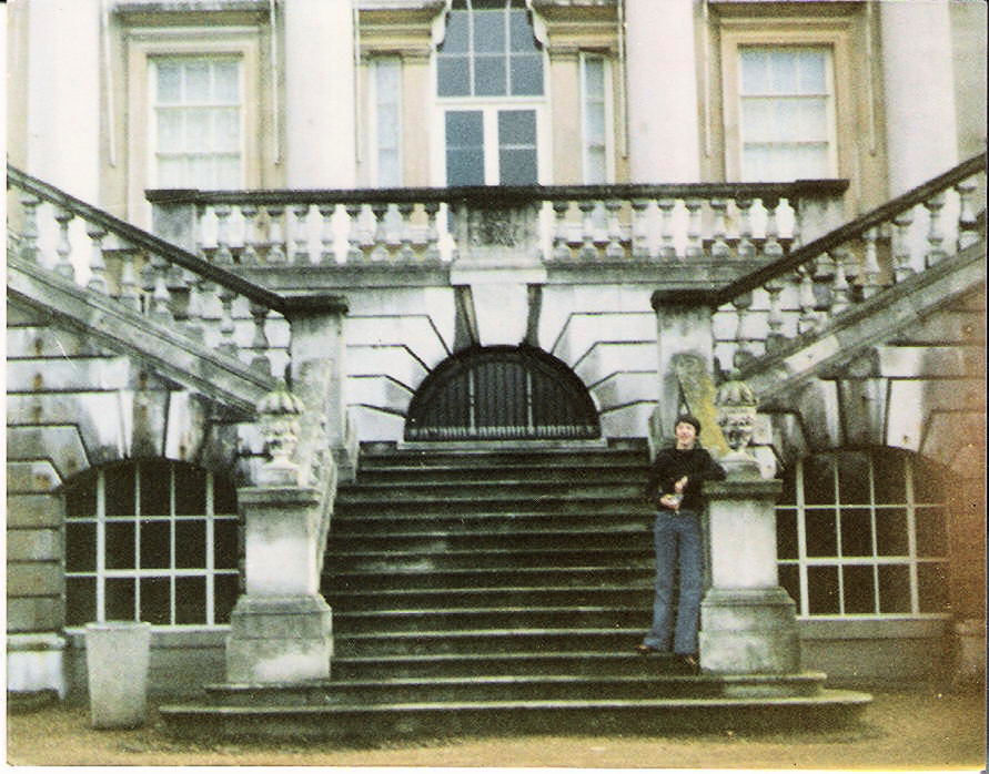100 stories: christopher saunders Christopher wears a black jumper and jeans while stand on the steps of white lodge. He leans on the left stair rail on the third step from the bottom.