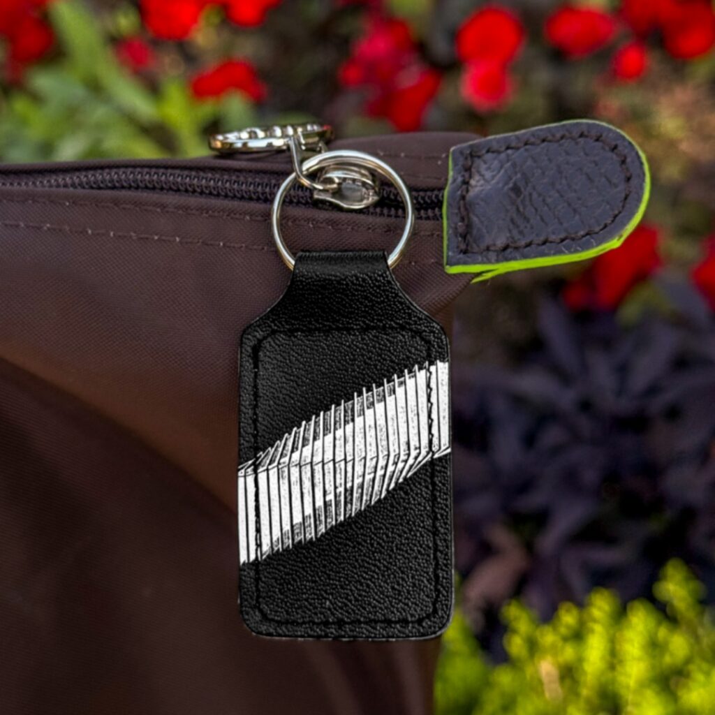 Behind the designs with centenary collection illustrators aimee tregunno and catja christensen A white sketch of the bridge of aspiration on a black background on a rounded rectangle keyring. The keyring is attached to a zipper on a black bag.