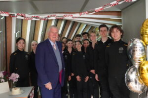 David stands in front of a group of upper school students wearing their black tracksuit uniforms.