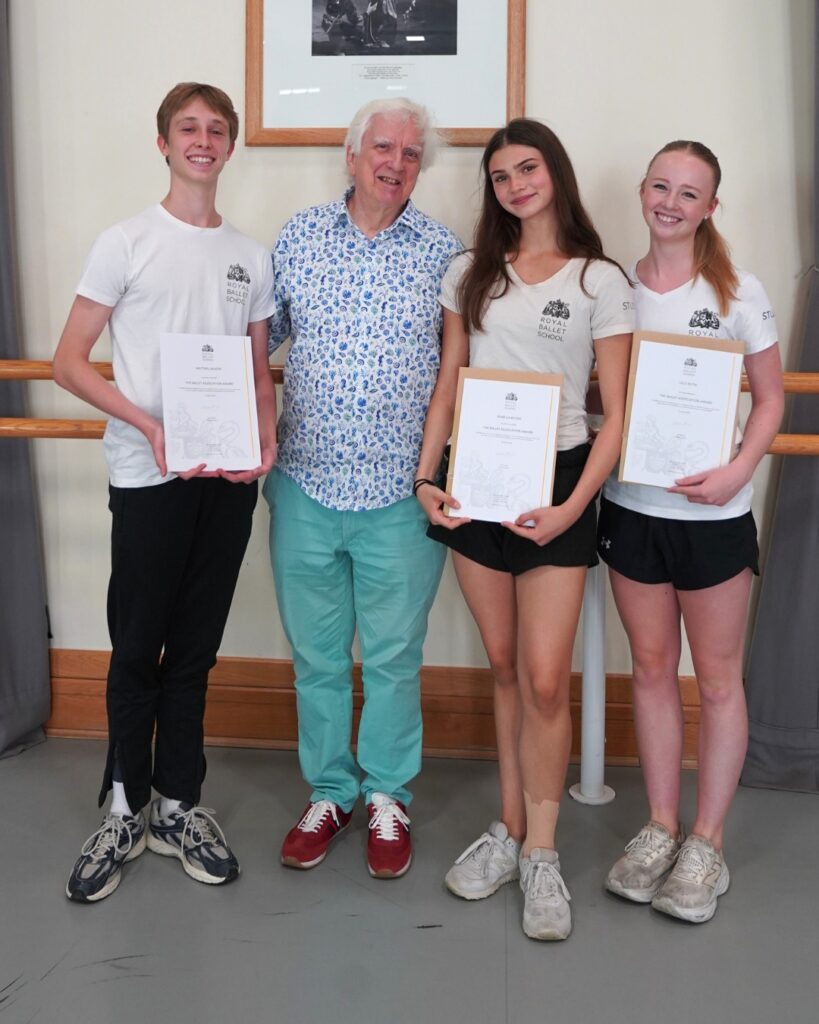 End-of-year celebrations and prize-giving ceremonies 2026 David bain stands with matthis, isabella and lilly, each holding their certificates. The girls wear white shirts and black shorts with light coloured trainers. Matthis wears a matching white shirt with black trousers and dark trainers.