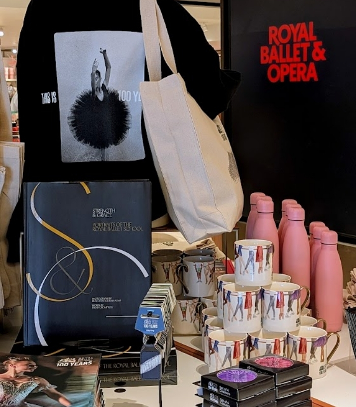 Behind the designs with centenary collection illustrators aimee tregunno and catja christensen A close up shot of the merchandise display table. Featured products are the tutu centenary cropped sweatshirt, grand défilé tote bag, through the years mugs, tutu coasters, centenary publications , bridge of aspiration keyrings and 100 years pink water bottles.