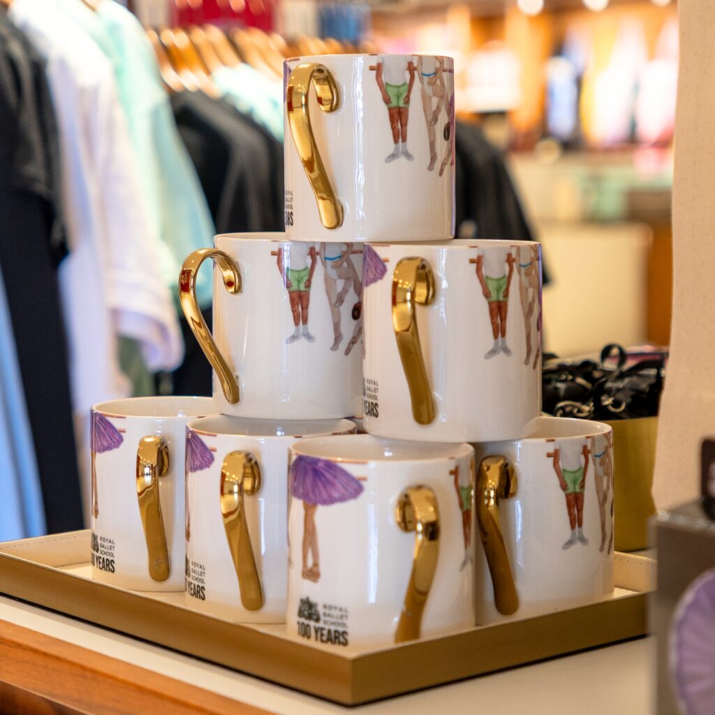 Behind the designs with centenary collection illustrators aimee tregunno and catja christensen A pyramid stack of mugs with gold handles at the royal opera house gift shop.