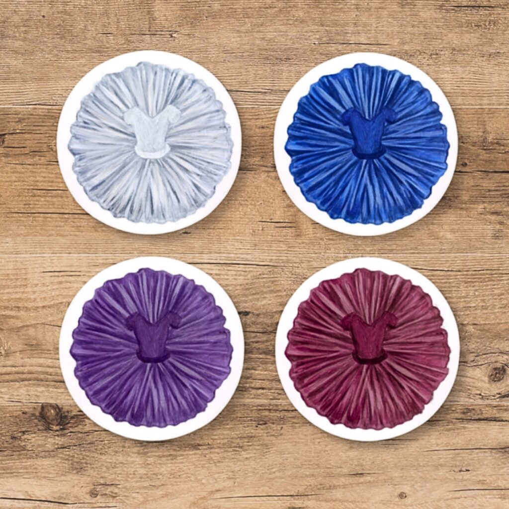 Behind the designs with centenary collection illustrators aimee tregunno and catja christensen Four circular tutu coasters in a square photographed from above on a light brown wooden surface. Counter clockwise from top left, the colours are white, blue, purple and red.