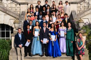 Year 11 students stand in a group on the stairs of white lodge in multicoloured gowns and suits.