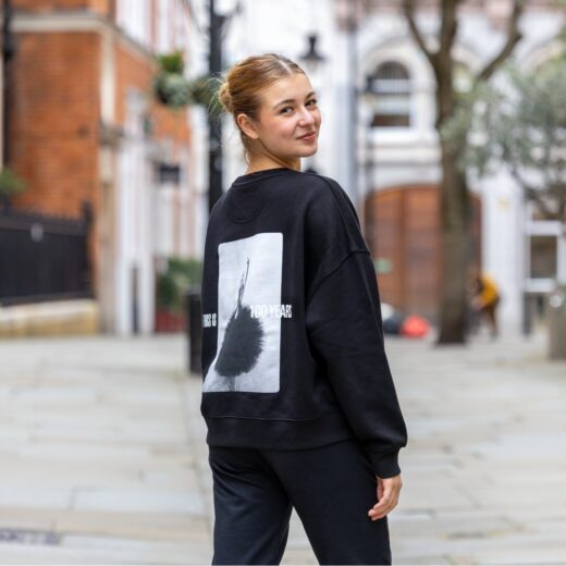 Product image of 'Centenary rehearsal sweatshirt' in black. Worn by a Royal Ballet School student in Upper School, Covent Garden. A collection of merchandise in celebration of 100 years of The Royal Ballet School.