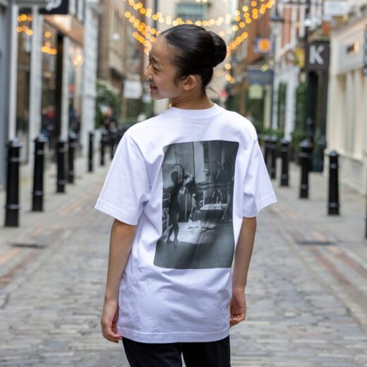 Product image of 'Centenary class t-shirt' in white. Worn by a Royal Ballet School student in Upper School, Covent Garden. A collection of merchandise in celebration of 100 years of The Royal Ballet School.