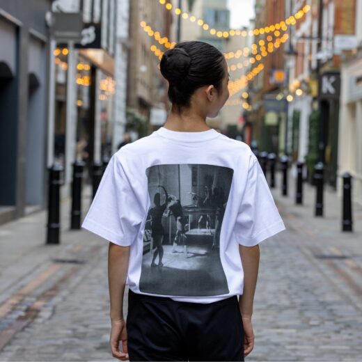 Product image of 'Centenary class t-shirt' in white. Worn by a Royal Ballet School student in Upper School, Covent Garden. A collection of merchandise in celebration of 100 years of The Royal Ballet School.