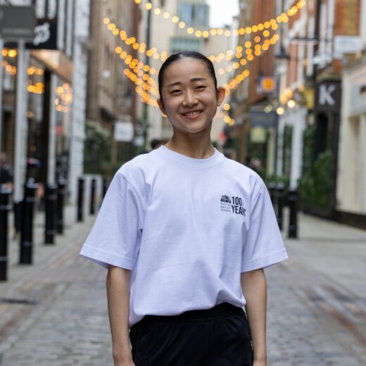 Product image of 'Centenary class t-shirt' in white. Worn by a Royal Ballet School student in Upper School, Covent Garden. A collection of merchandise in celebration of 100 years of The Royal Ballet School.