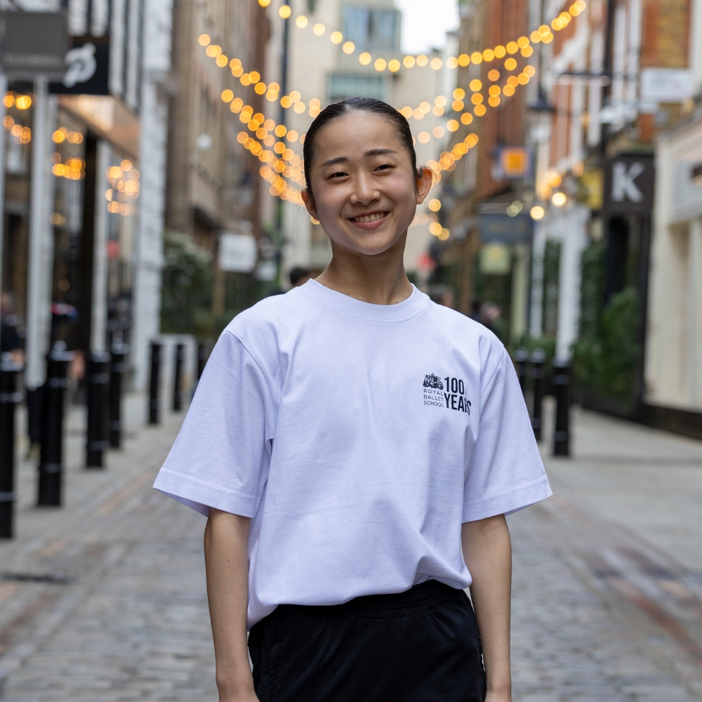 At the barre centenary oversized t-shirt Product image of 'centenary class t-shirt' in white. Worn by a royal ballet school student in upper school, covent garden. A collection of merchandise in celebration of 100 years of the royal ballet school.