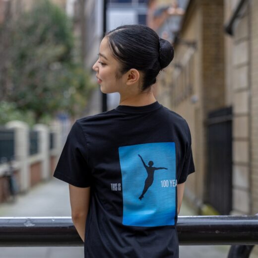 Product image of 'Centenary performance children's t-shirt' in black. Worn by a Royal Ballet School student in Upper School, Covent Garden. A collection of merchandise in celebration of 100 years of The Royal Ballet School.