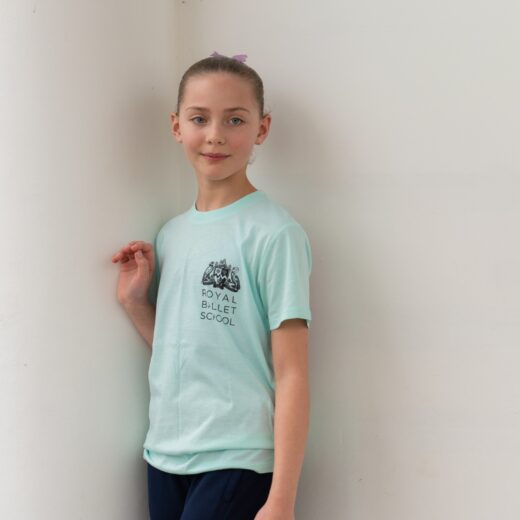 Product image of 'Centenary performance children's t-shirt' in mint. Worn by a Royal Ballet School student at White Lodge. A collection of merchandise in celebration of 100 years of The Royal Ballet School.
