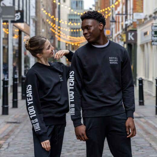 Product image of 'This is 100 years sweatshirt' in black. Worn by Royal Ballet School students in Upper School, Covent Garden. A collection of merchandise in celebration of 100 years of The Royal Ballet School.