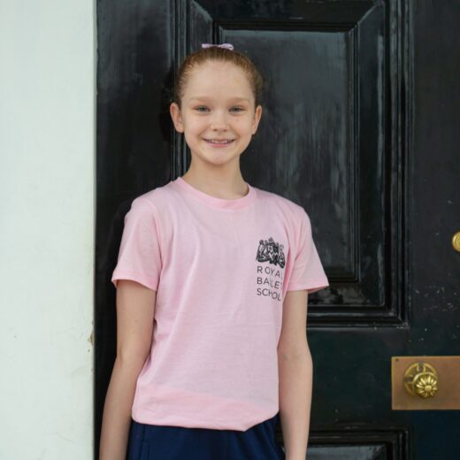 Product image of 'This is 100 years children's t-shirt' in pink. Worn by a Royal Ballet School student at White Lodge. A collection of merchandise in celebration of 100 years of The Royal Ballet School.