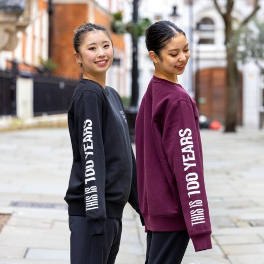 Product image of 'This is 100 years sweatshirt' in black and burgundy. Worn by Royal Ballet School students in Upper School, Covent Garden. A collection of merchandise in celebration of 100 years of The Royal Ballet School.