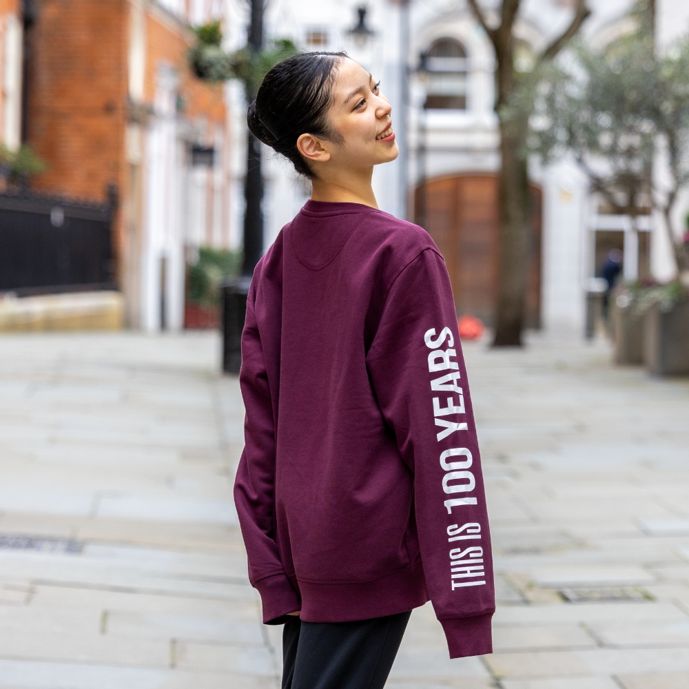 This is 100 years sweatshirt Product image of 'this is 100 years' sweatshirt in burgundy. Worn by a royal ballet school student in upper school, covent garden. A collection of merchandise in celebration of 100 years of the royal ballet school.