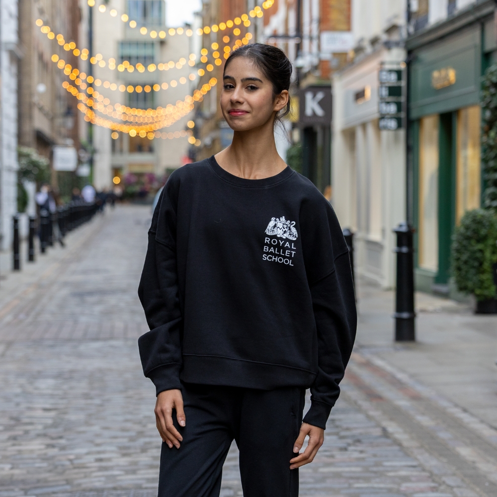 Tutu centenary cropped sweatshirt Product image of 'centenary rehearsal sweatshirt' in black. Worn by a royal ballet school student in upper school, covent garden. A collection of merchandise in celebration of 100 years of the royal ballet school.