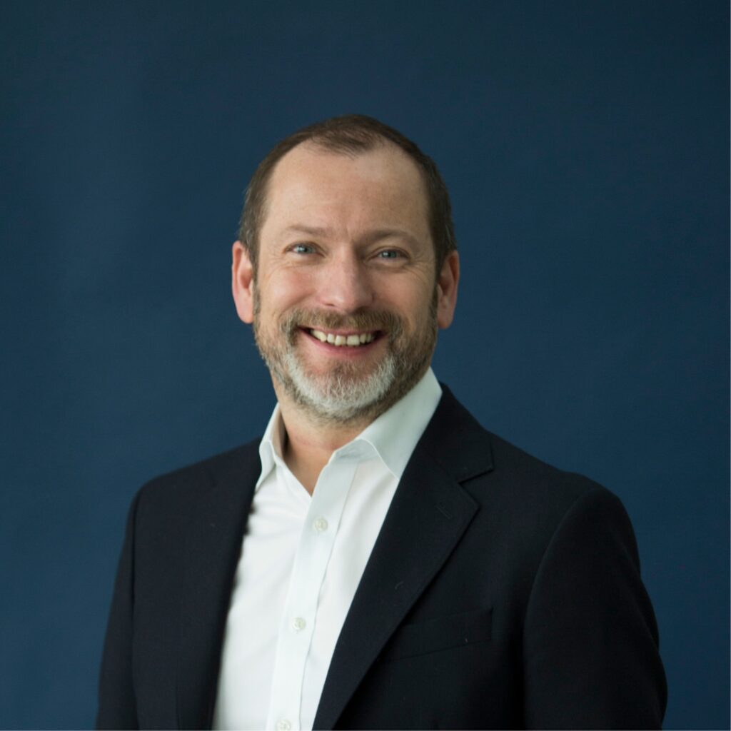Kevin o'hare smiles at the camera. He wears a white button down shirt and black jacket.