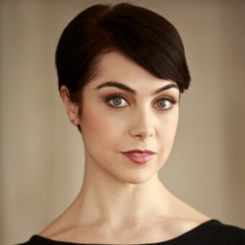 Leanne cope looks at the camera with a slight smile. She wears a wide neck black top.