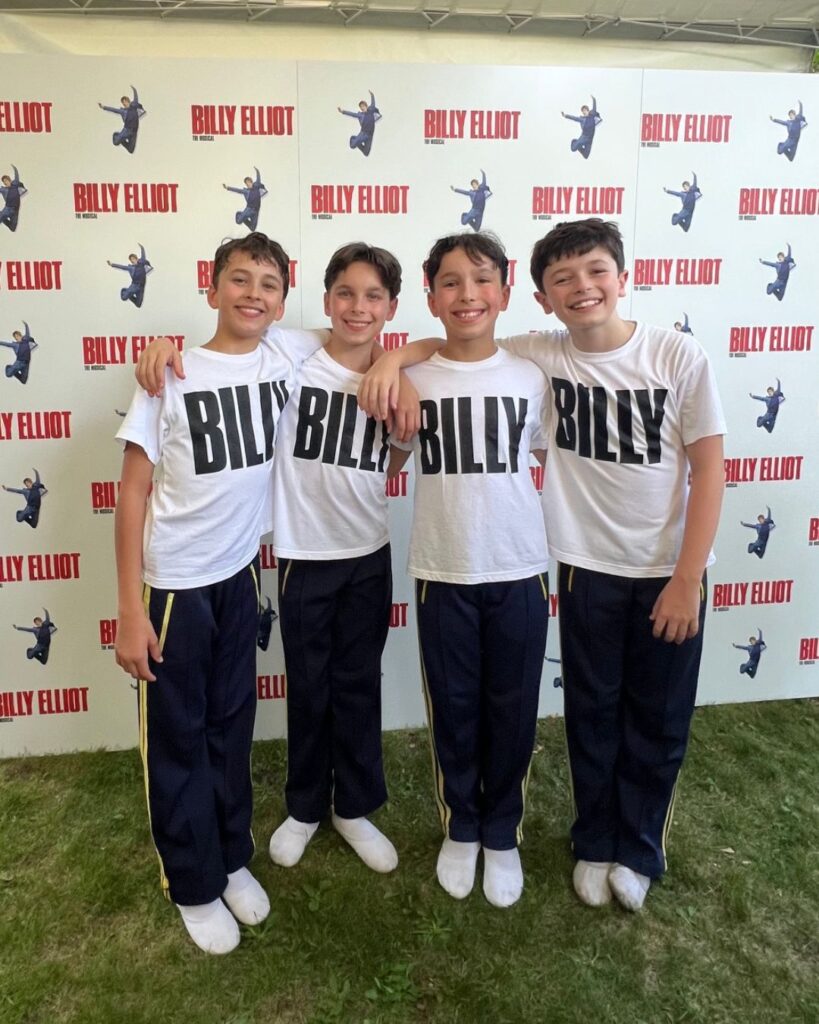 Year 8 student rafferty on starring as the titular role in billy elliot the musical The four billys stand in front of a wall that has the billy elliot the musical logo printed repeatedly.