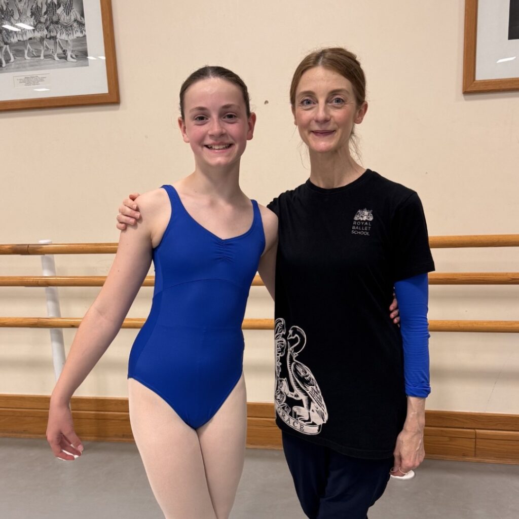 Mid associate students share what they love about the associate programme Grace stands with amber doyle in the studio. She wears a blue leotard and pink tights. Amber wears a black rbs t-shirt with a blue long-sleeve shirt underneath.