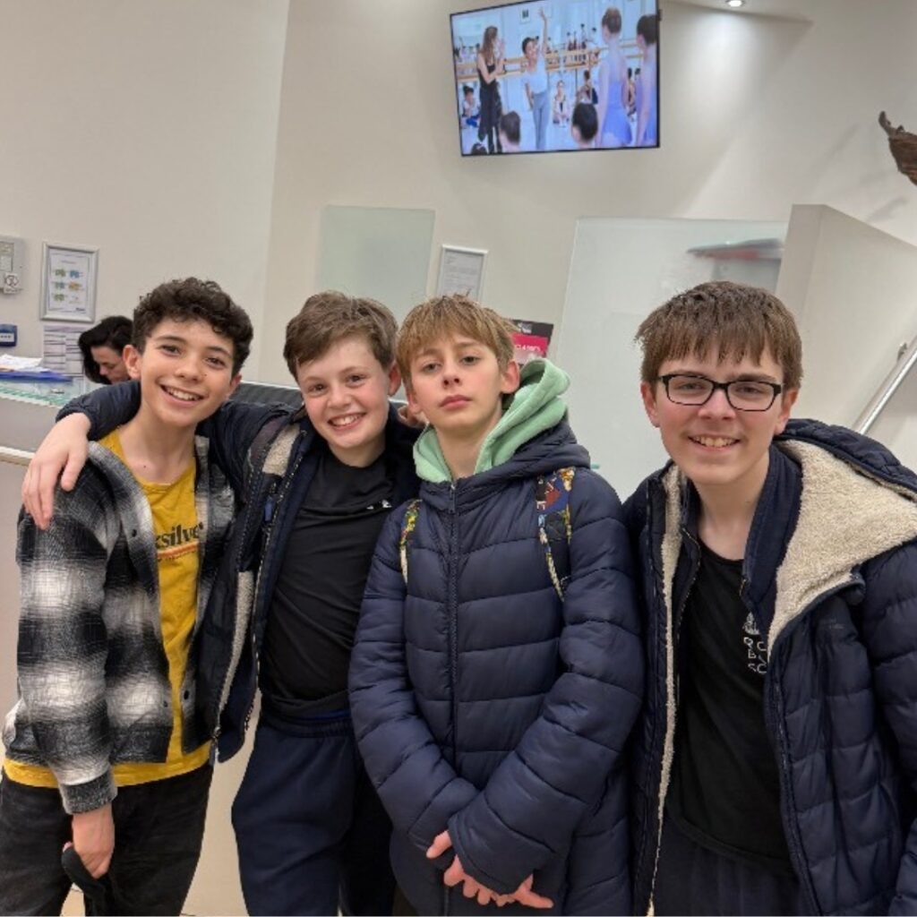 Mid associate students share what they love about the associate programme Joshua stands with friends in winter coats in the reception area at upper school.