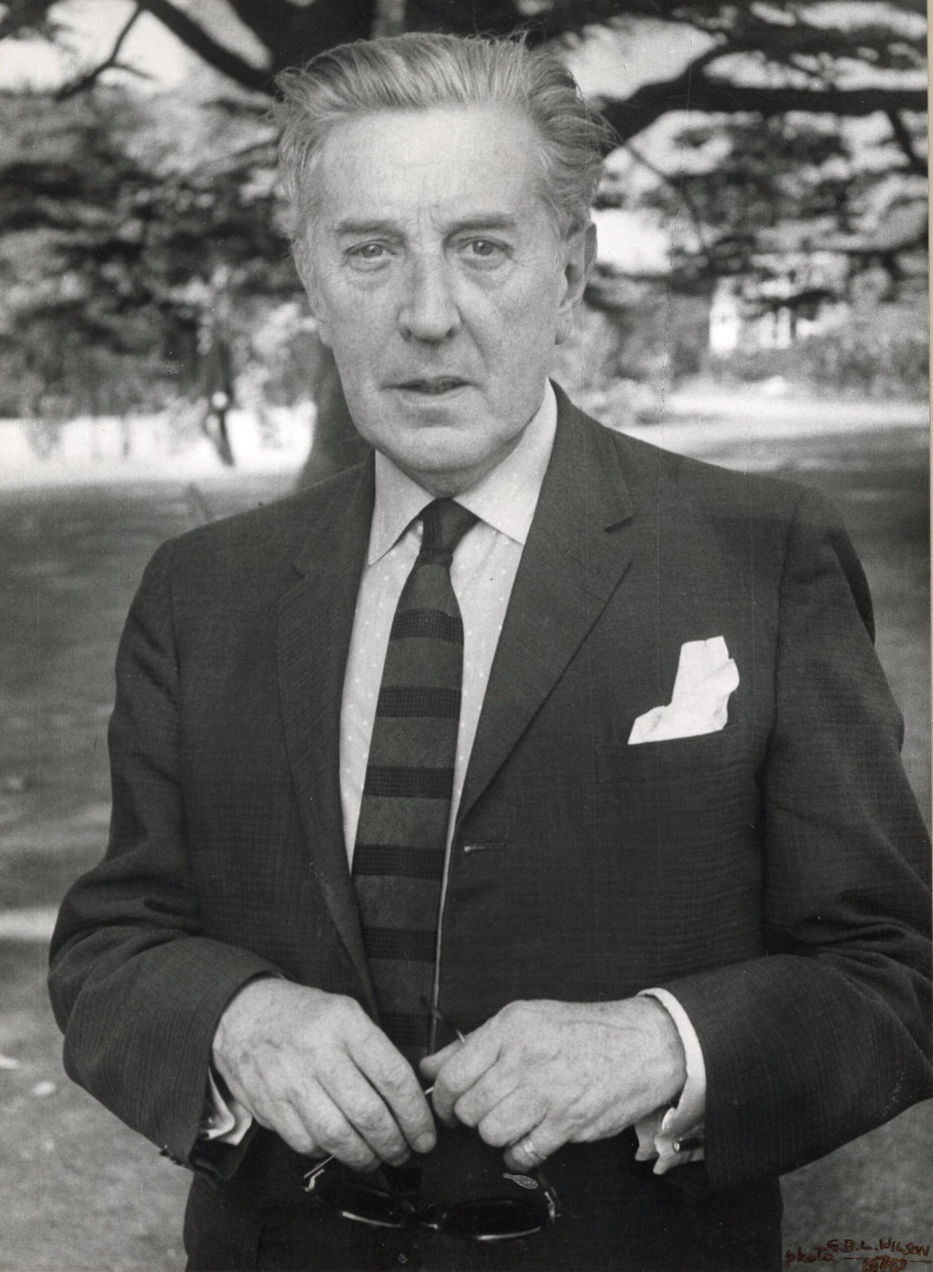 100 stories: frederick ashton Ashton wears a black suit and stands in front of a tree at white lodge. He was director of the royal ballet at the time.