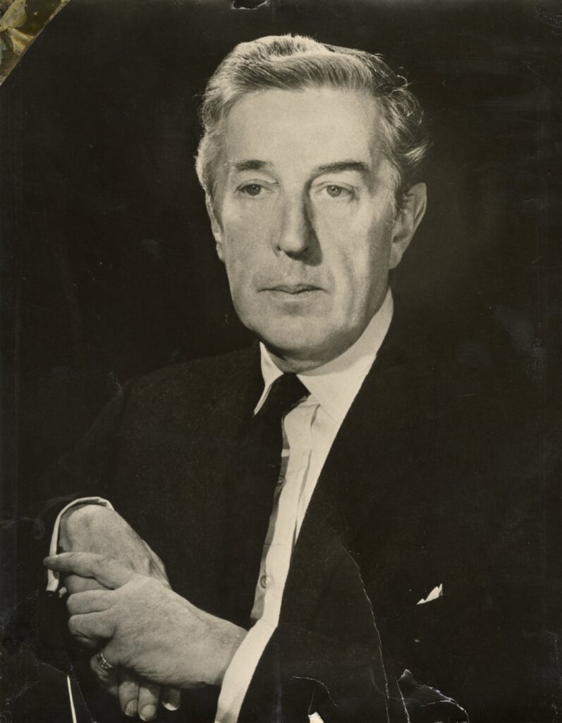 100 stories: frederick ashton Frederick ashton sits on a chair against a black backdrop with his right arm draped over the chair back and his left hand holding his right. He looks just off to the right of the camera with a neutral expression.