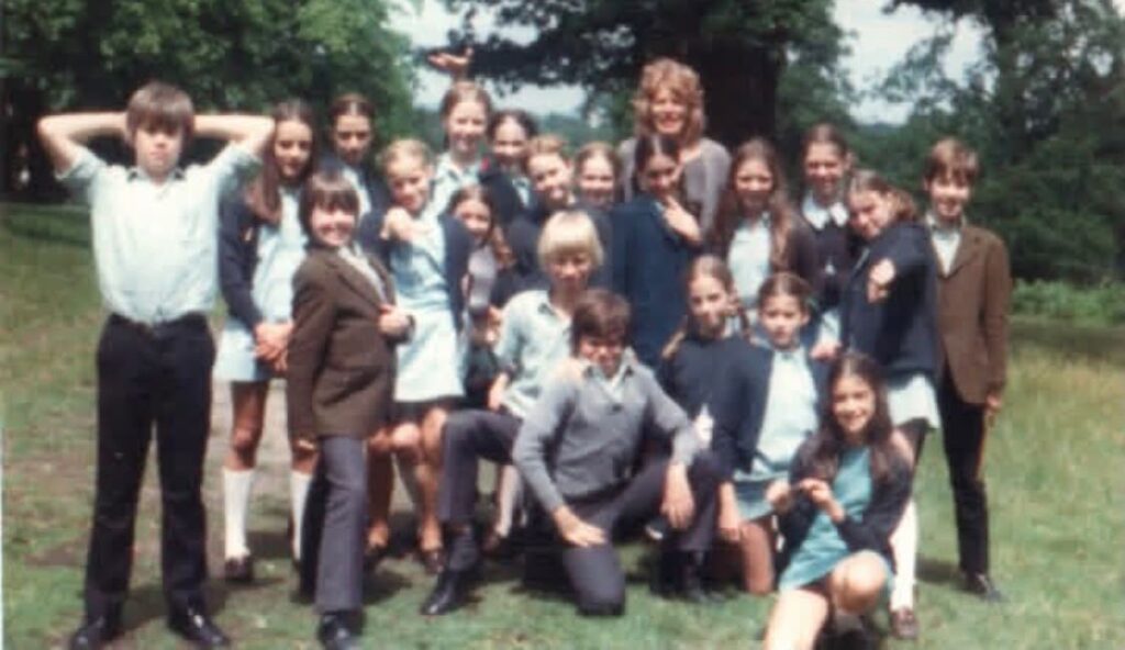 A group photo of students outside of white lodge. Rachel crouches in the front row with her straight brown hair hanging down.